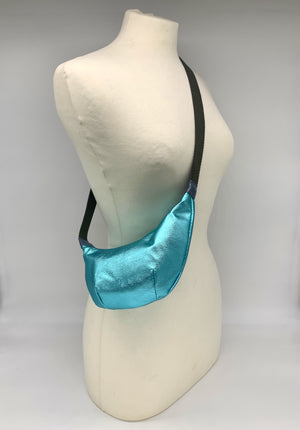 Small crossbody bag in electric turquoise leather worn across a mannequin