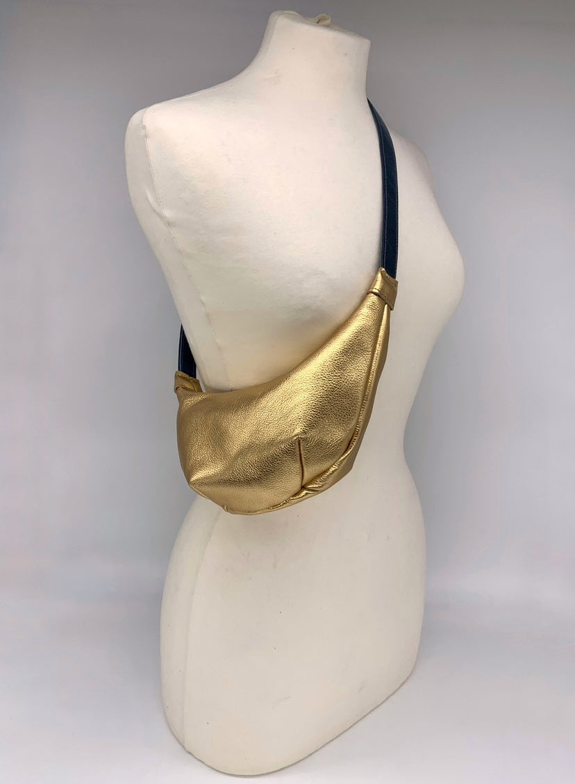 Small crossbody bag in gold leather worn across a mannequin